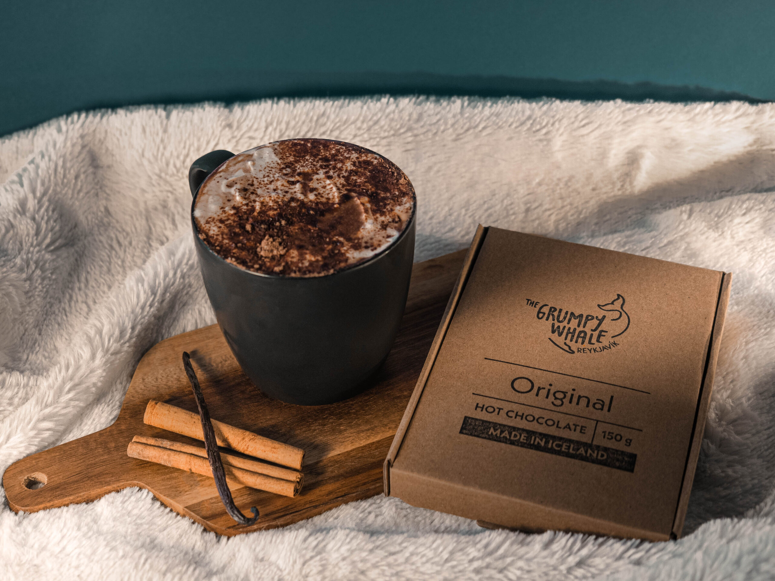 The Grumpy Whale Original Hot Chocolate has notes or vanilla and cinnamon. This serving suggestion with oat milk, cream and cocoa dusting on a blanket displays how tasty and cosy our products can be.